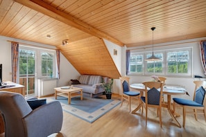 A cozy living room with a sloped ceiling, a sofa, a coffee table, and a dining area with chairs and a table.