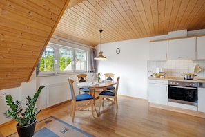 A modern kitchen with wooden ceiling beams, a dining area with blue chairs, and a potted plant.