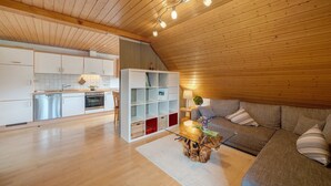 Een modern interieur met een keuken, een eethoek en een woonkamer, met houten plafonds en een inbouwboekenplank.