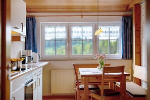A kitchen with a dining table, chairs, a hanging light fixture, and a window with curtains. - Apartment 'Vogelsang' with Shared Garden, Balcony and Wi-Fi (St Peter)