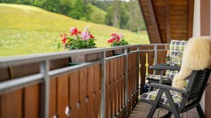 Een balkon met uitzicht op een groen veld, een tafel met stoelen en een fles drank.
