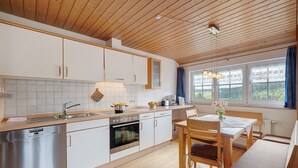 Een moderne keuken met houten kastjes, een vaatwasser, een oven en een eethoek met een tafel en stoelen.