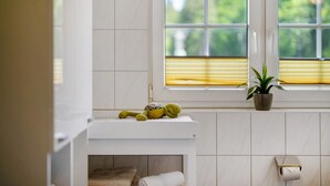 Een badkamer met een toilet, een handdoekrek, een handdoek, een toiletrolhouder en een raam met jaloezieën.