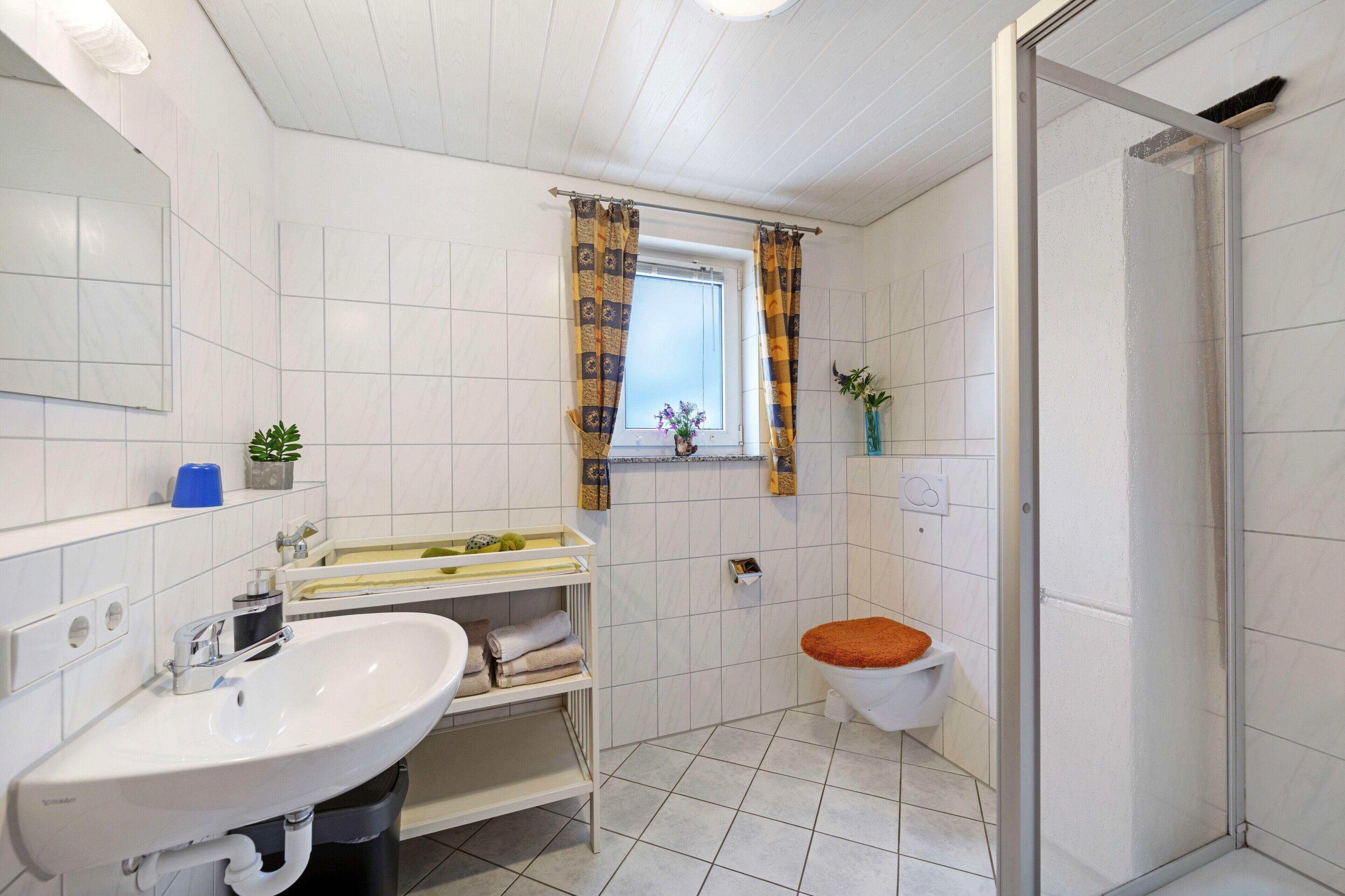 Une salle de bain équipée d’un lavabo, de toilettes, d’une douche et d’une fenêtre avec des rideaux.