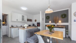 A modern kitchen with white cabinetry, a central island, and a dining area with a wooden table and gray upholstered chairs.