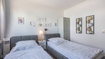Una camera d'albergo con due letti, un comodino con una lampada, un armadio e decorazioni a parete tra cui quadri incorniciati e un ornamento a forma di cuore.