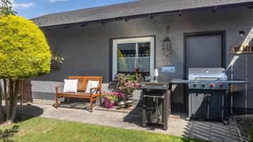 Eine Terrasse mit einer Holzbank, einem Grill und Kübelpflanzen.