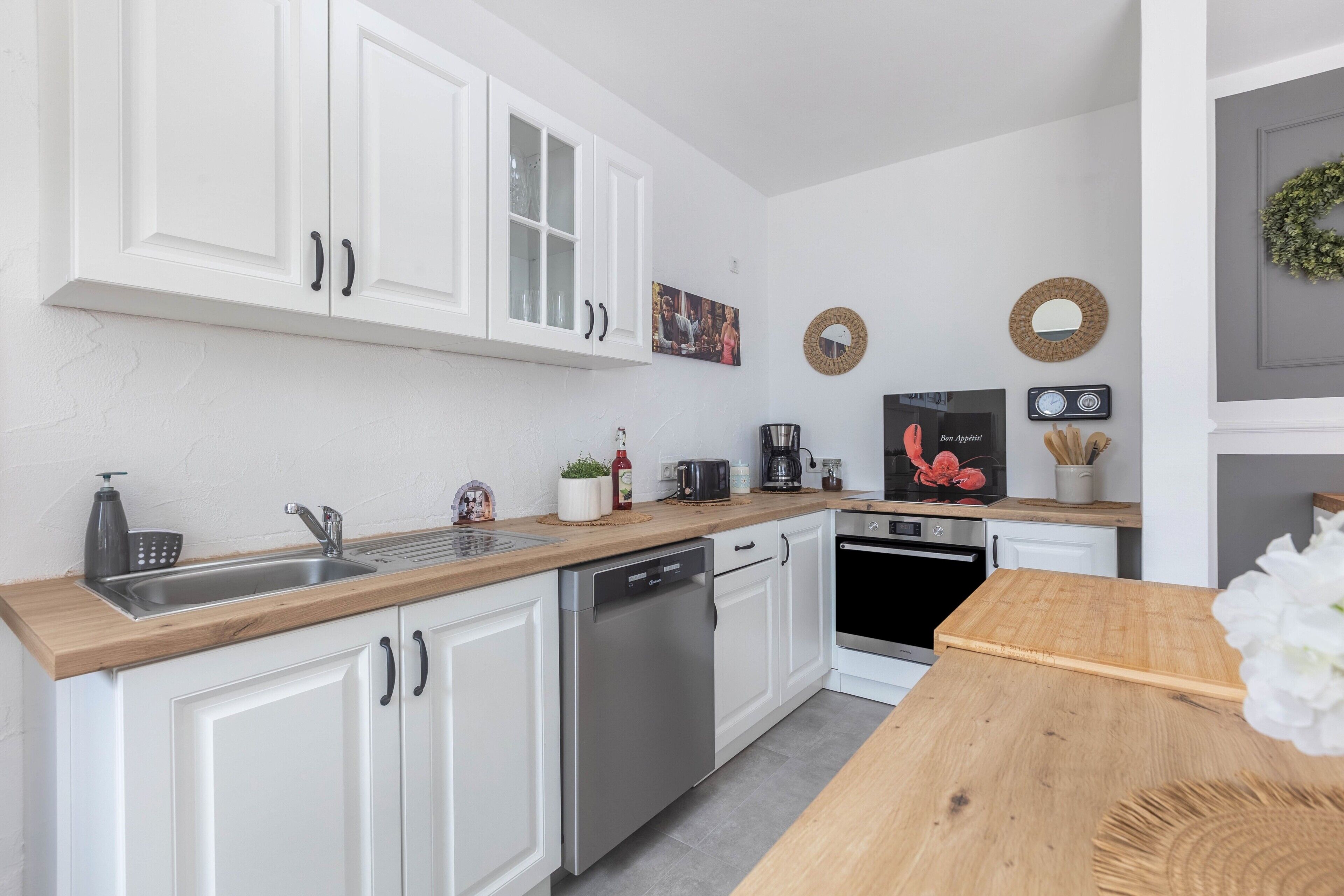 A modern kitchen with white cabinets, stainless steel appliances, and a wooden countertop.