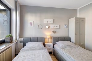 A twin bedroom with two beds, a bedside table with a lamp, a wardrobe, and a window with a plant. - Apartment 'Riekes' with Mountain View, Private Terrace and Wi-Fi (Schmallenberg)