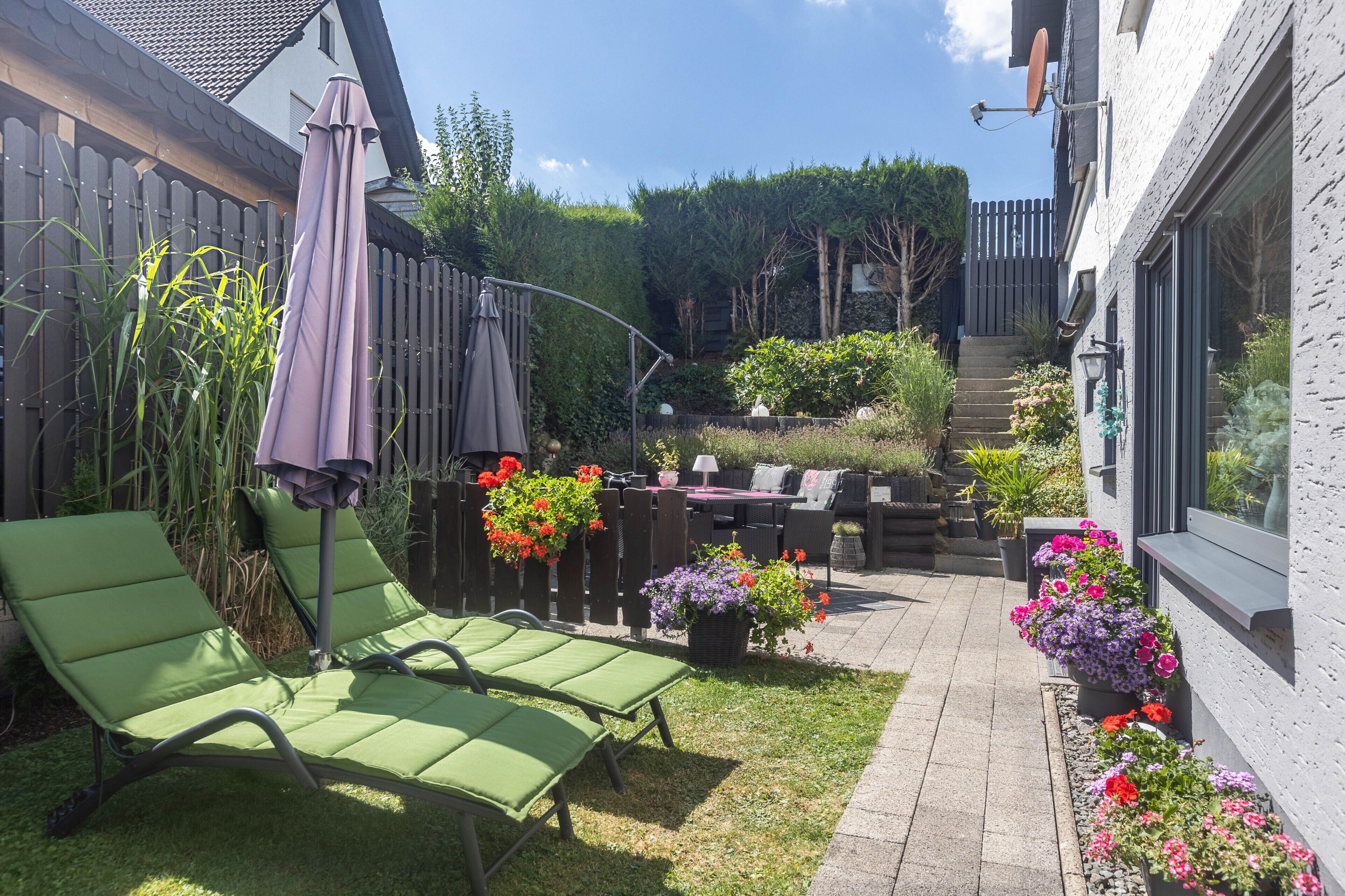 A patio area with green lounge chairs, a wooden fence, and potted plants.
