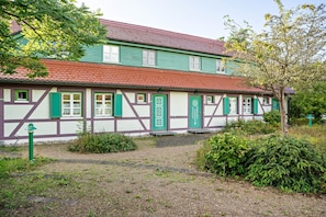 Ett traditionellt hus med korsvirkesfasad, ett rött tegeltak, gröna fönsterluckor och en grusgång som leder fram till entrén.