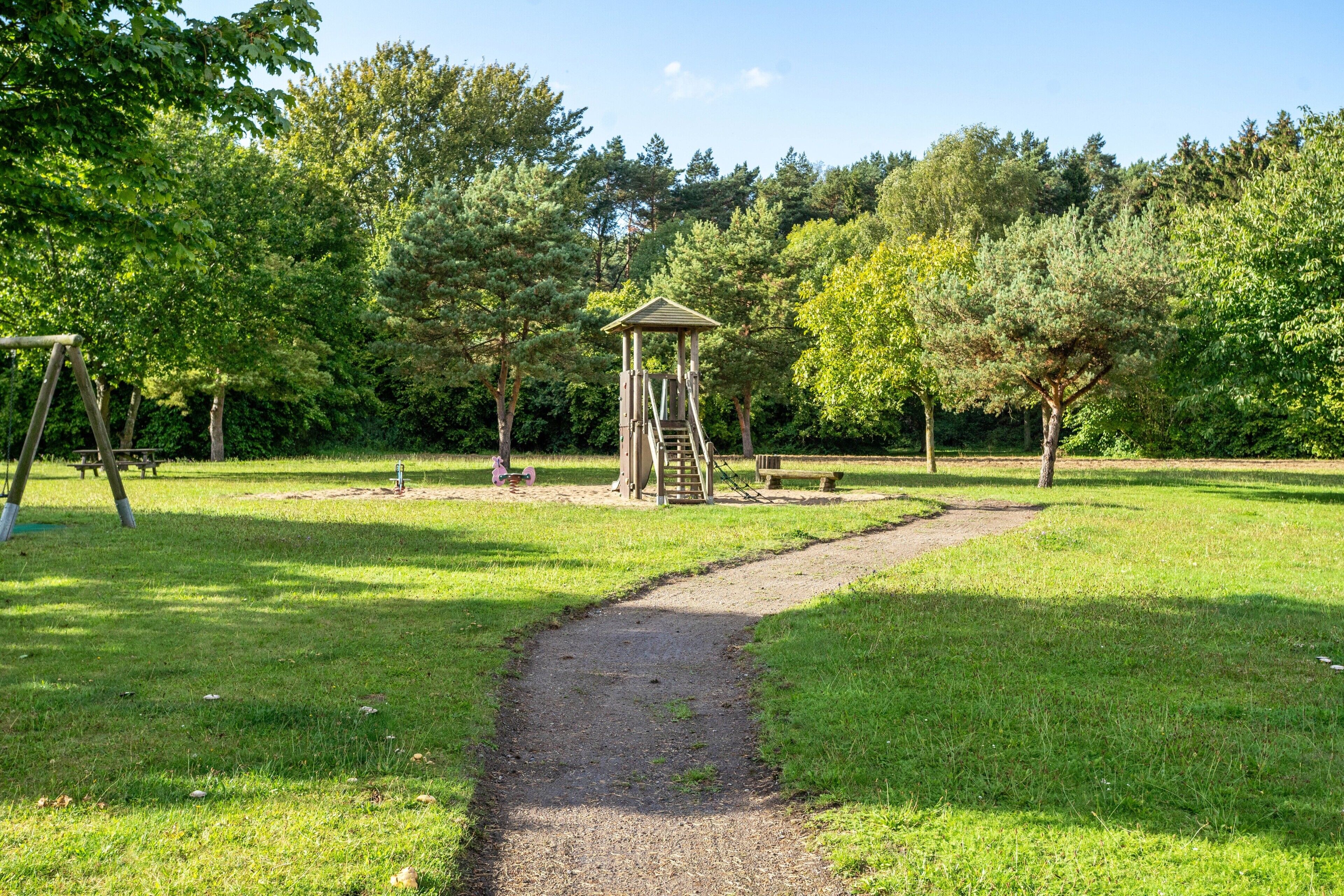 Ein Park mit einer hölzernen Spielanlage, einem Picknickbereich und einem gut ausgebauten Weg.