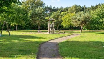 Ein Park mit einer hölzernen Spielanlage, einem Picknickbereich und einem gut ausgebauten Weg.