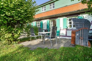 Un bâtiment à la façade verdoyante, au toit rouge et doté d’un patio aménagé avec du mobilier d’extérieur.