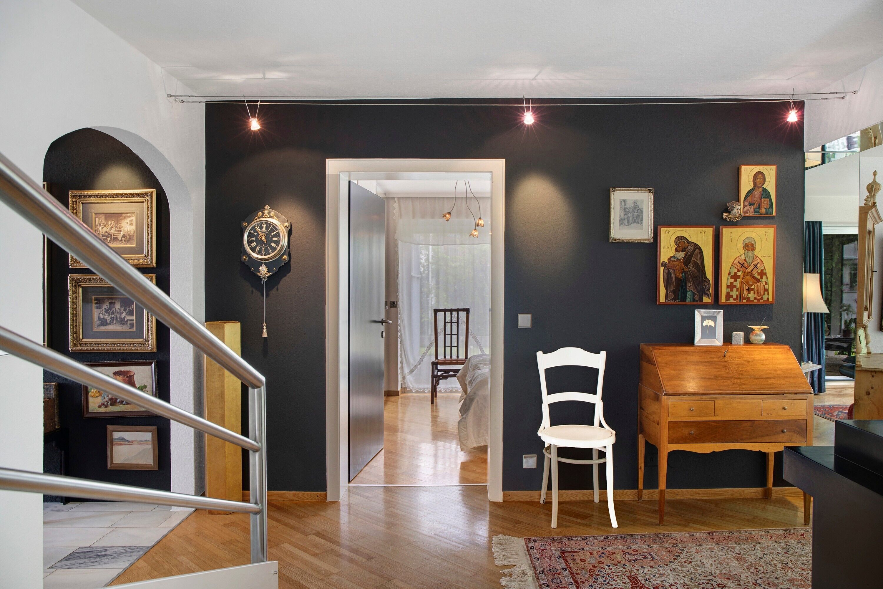 A room with a staircase, a wooden floor, a white chair, a wooden cabinet, and a bed with a white canopy.