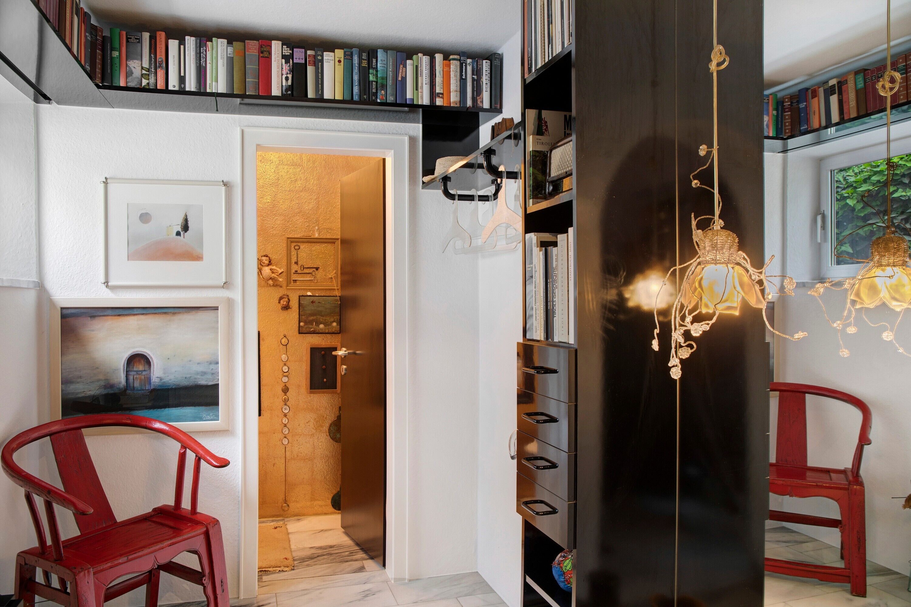 A room with a bookshelf, a red chair, a door with a golden handle, and a hanging light fixture.