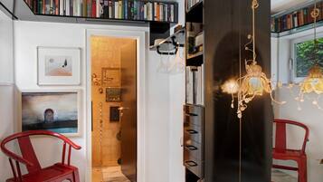 A room with a bookshelf, a red chair, a door with a golden handle, and a hanging light fixture.
