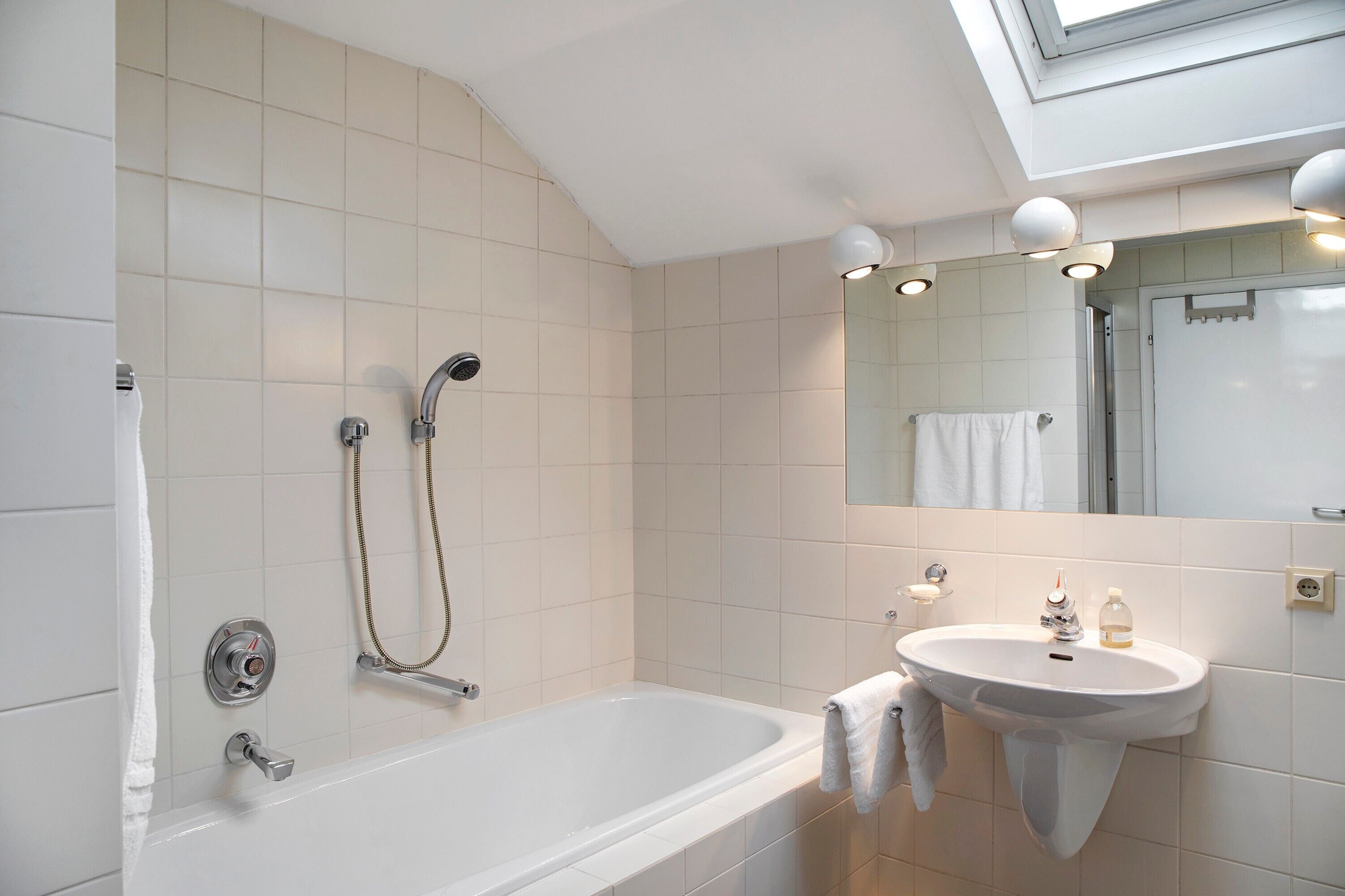 Une salle de bain équipée d’une baignoire, d’un lavabo, d’un miroir et d’une pomme de douche.