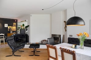 A modern living room with a fireplace, black leather chairs, a dining table with a white tablecloth, and a large black pendant light. - Haus Gutschi with Mountain Views, Large Garden and Wi-Fi (Gemeinde Imst)
