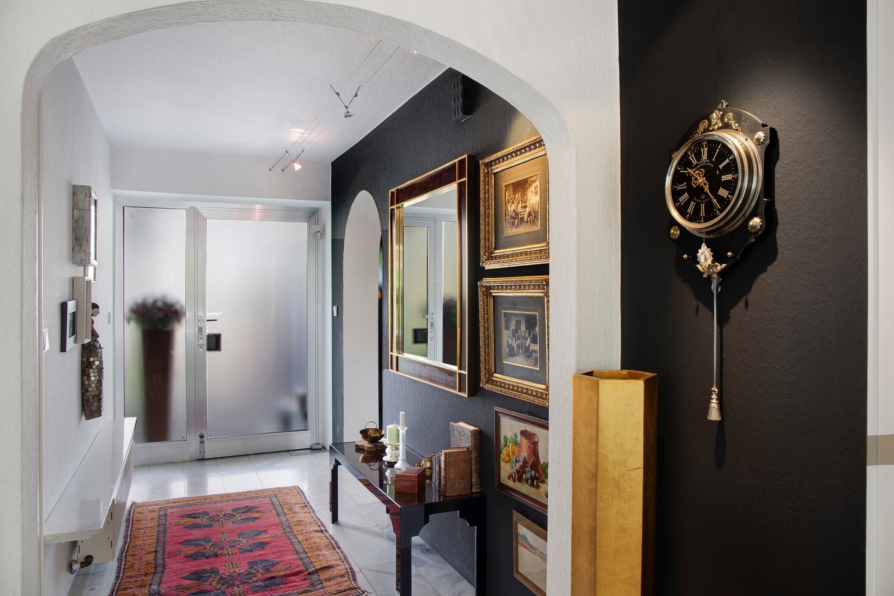 Un couloir avec un mur noir, une grande horloge et des tableaux encadrés.