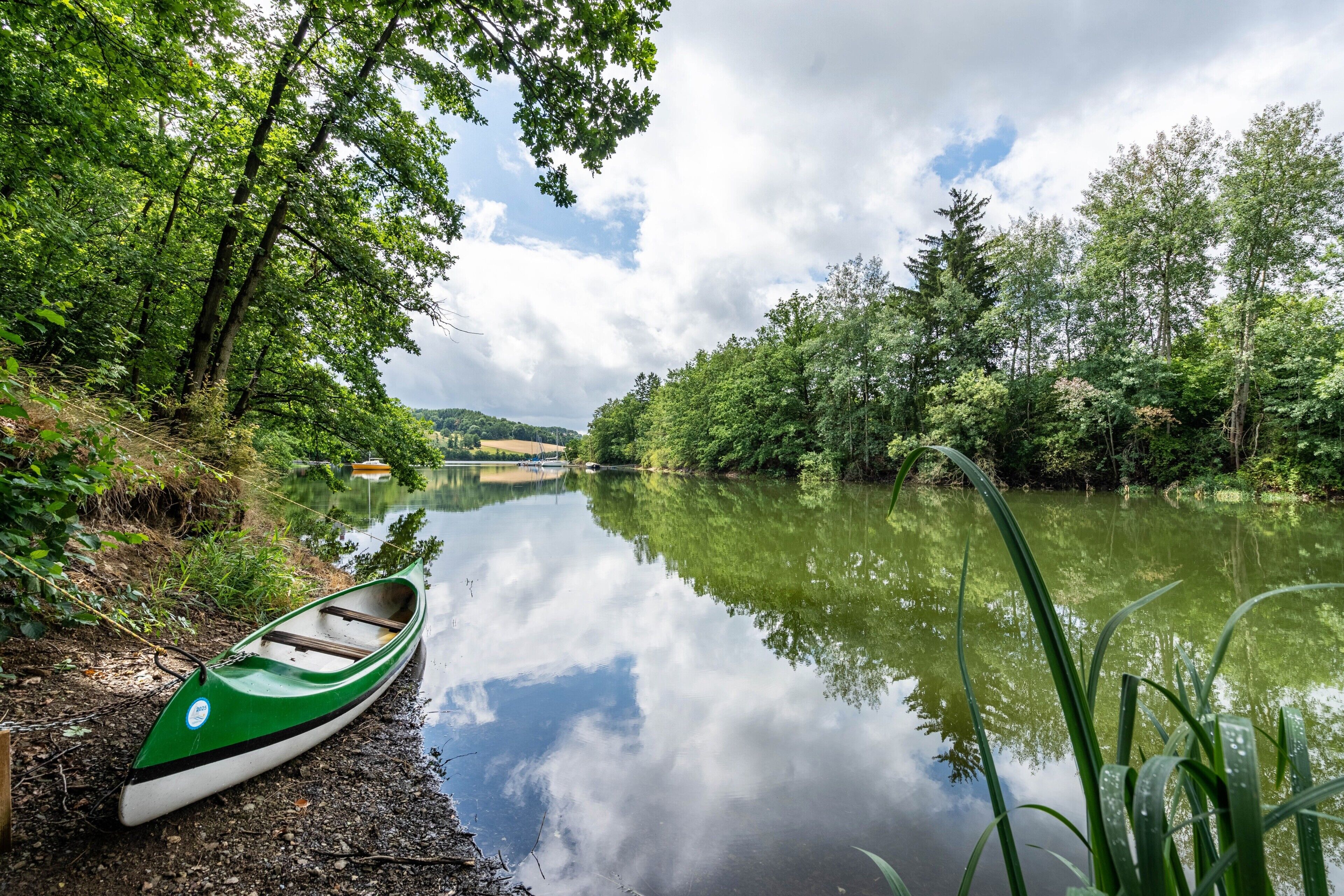 Ein ruhiger Fluss mit einem grünen Kanu, das an einem Steg festgemacht ist, umgeben von üppigem Grün.