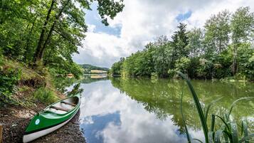Ein ruhiger Fluss mit einem grünen Kanu, das an einem Steg festgemacht ist, umgeben von üppigem Grün.
