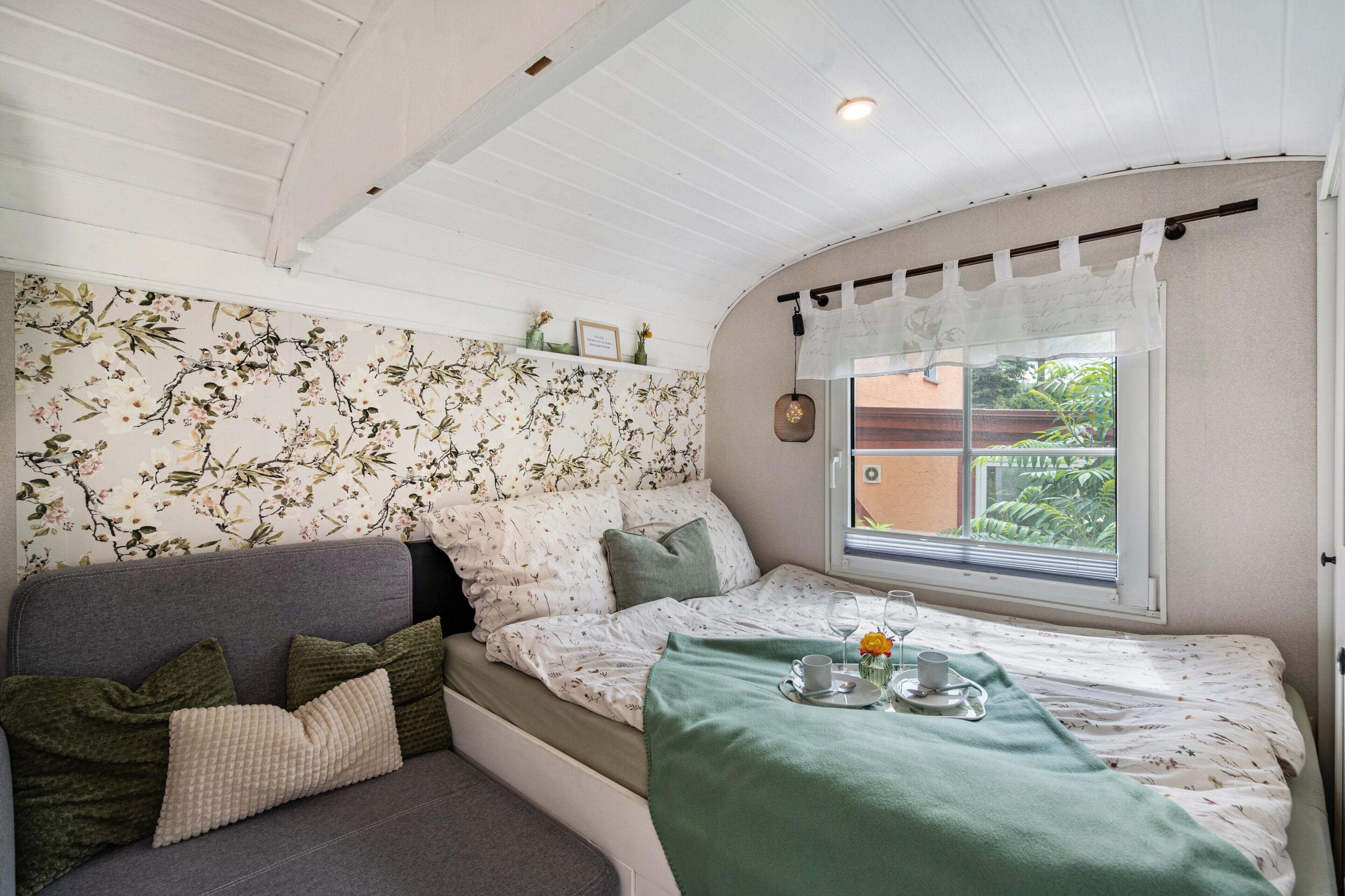 Una habitación acogedora con cama, sofá, ventana con vistas a vegetación y techo con vigas de madera.