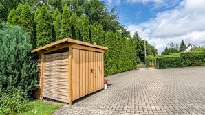 A wooden shed with a slatted roof, surrounded by greenery and a paved driveway. - Tiny Home 'Amselnest' with Lake View, Private Terrace, and Wi-Fi (Oelsnitz/Vogtl.)