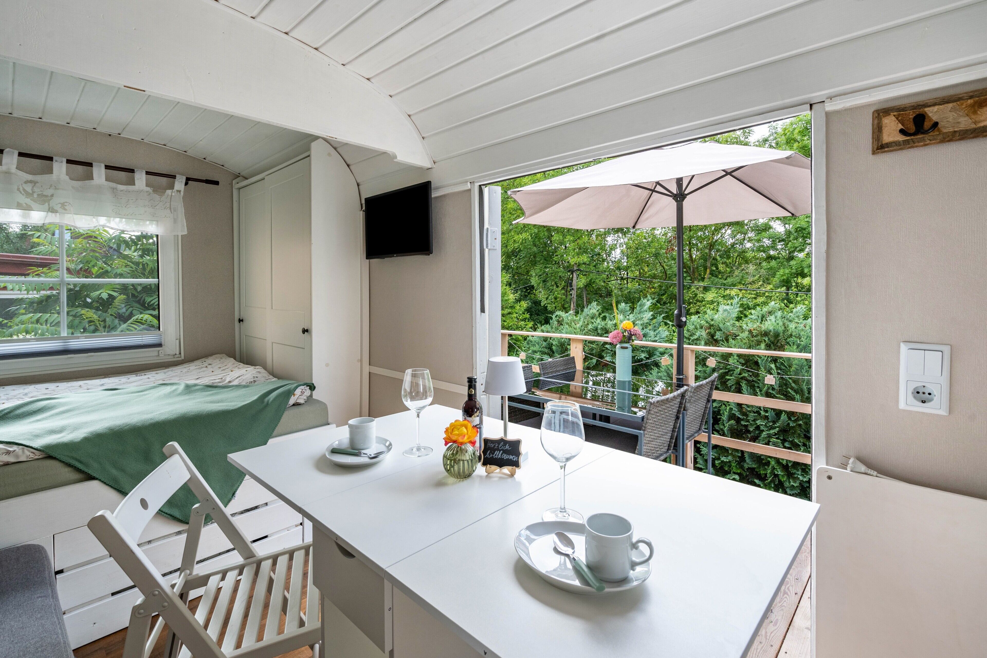Una habitación con cama, una mesa con silla, un ventanal con vistas a zonas verdes, y un televisor de pared.