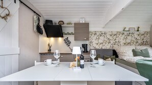 A compact room with a dining table, two chairs, a small kitchen area, and a bed with floral wallpaper. - Tiny Home 'Amselnest' with Lake View, Private Terrace, and Wi-Fi (Oelsnitz/Vogtl.)
