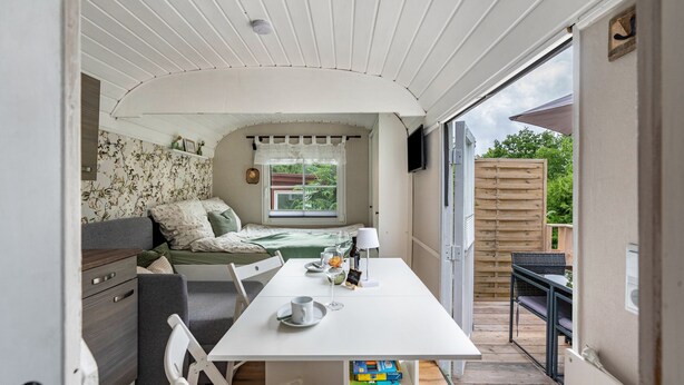 A cozy room with a bed, a table with a lamp, and a window with curtains. - Tiny Home 'Amselnest' with Lake View, Private Terrace, and Wi-Fi (Oelsnitz/Vogtl.)