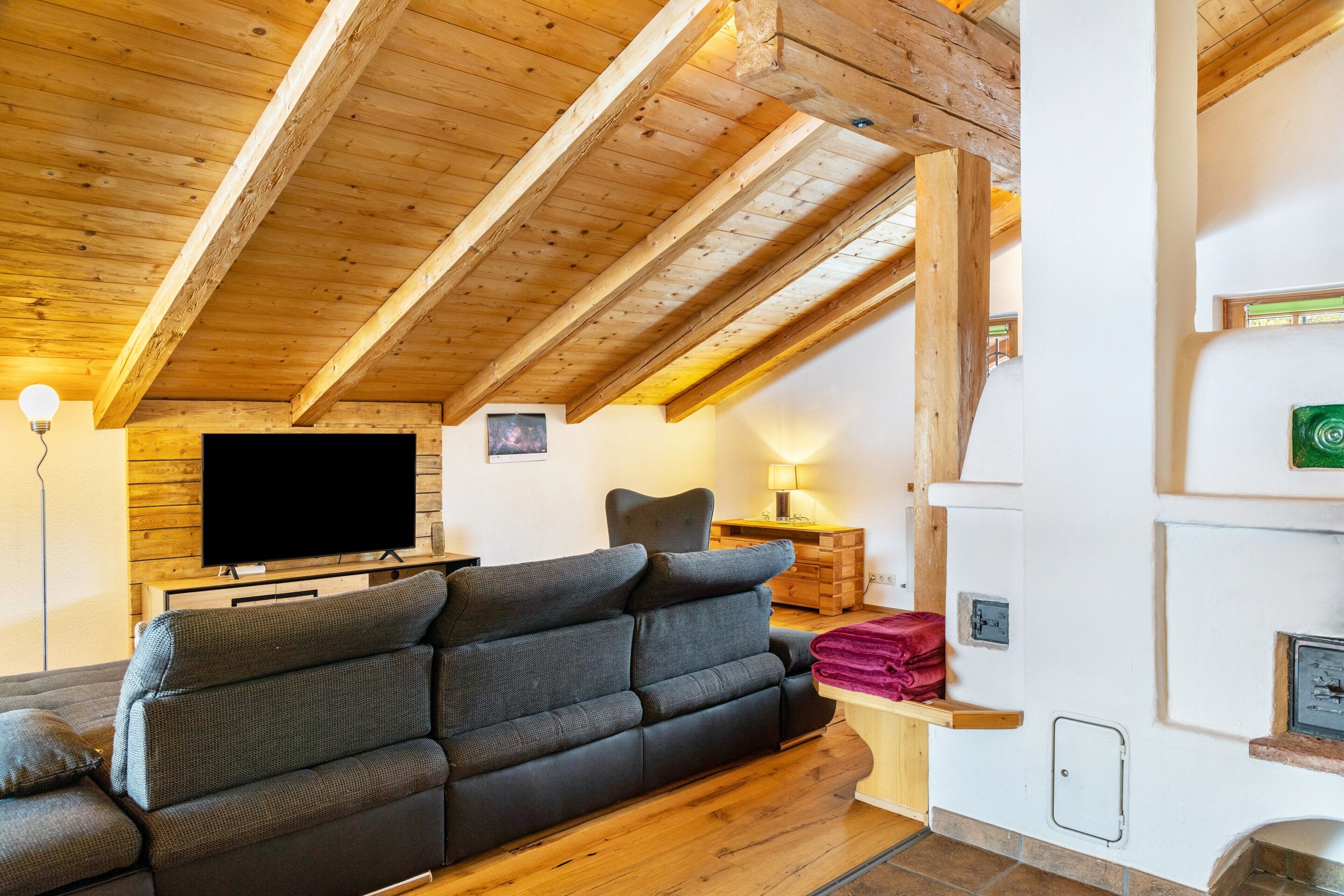 A cozy living room with a wooden ceiling, a flat-screen TV, a sofa, a chair, and a fireplace.