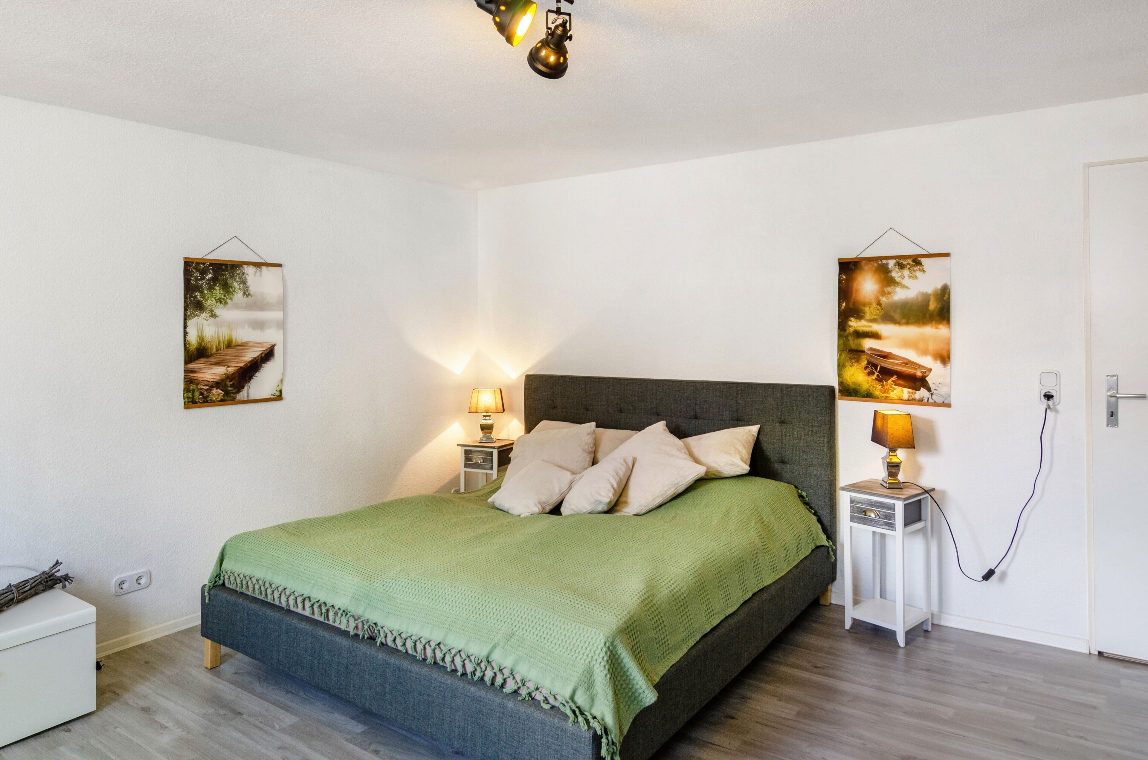 A bedroom with a bed, bedside lamps, a nightstand, and two wall-mounted pictures.