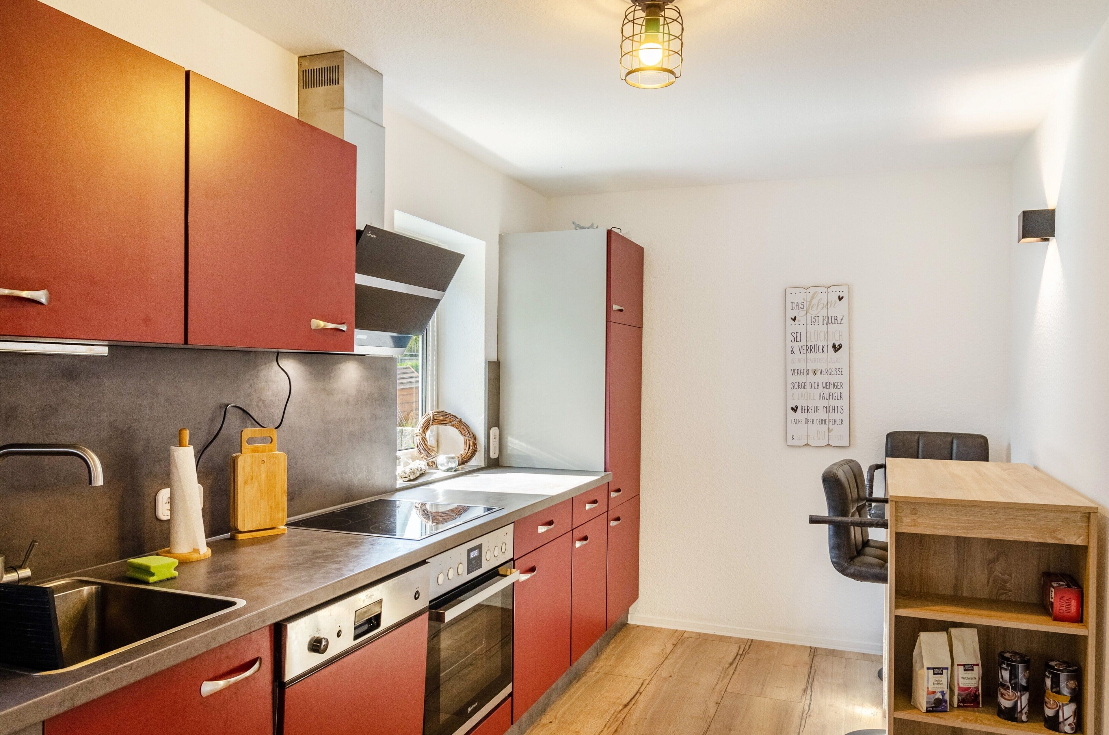 Una cocina con armarios rojos, un lavamanos de acero inoxidable y una estantería de madera con café y bolsas.