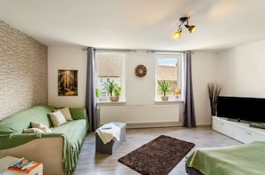A modern living room with a brick wall, a green sofa, a flat-screen TV, and two windows with curtains.