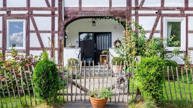 A traditional half-timbered house with a wooden gate, potted plants, and a clear sky.