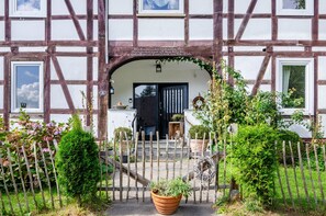 A traditional half-timbered house with a wooden gate, potted plants, and a clear sky.