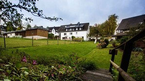 A residential area with a grassy yard, a wooden staircase, and houses with sloped roofs. - Apartment 'Kornkammer' with Shared Garden, Balcony and Wi-Fi (Schmallenberg)