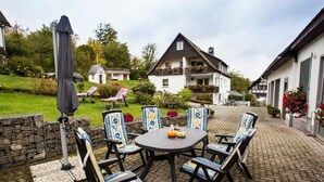A patio with a round table and chairs, a covered umbrella, and a stone wall. - Apartment 'Kornkammer' with Shared Garden, Balcony and Wi-Fi (Schmallenberg)