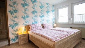 A bedroom with a bed, a nightstand, a lamp, a window, and a wardrobe. - Apartment 'Kornkammer' with Shared Garden, Balcony and Wi-Fi (Schmallenberg)