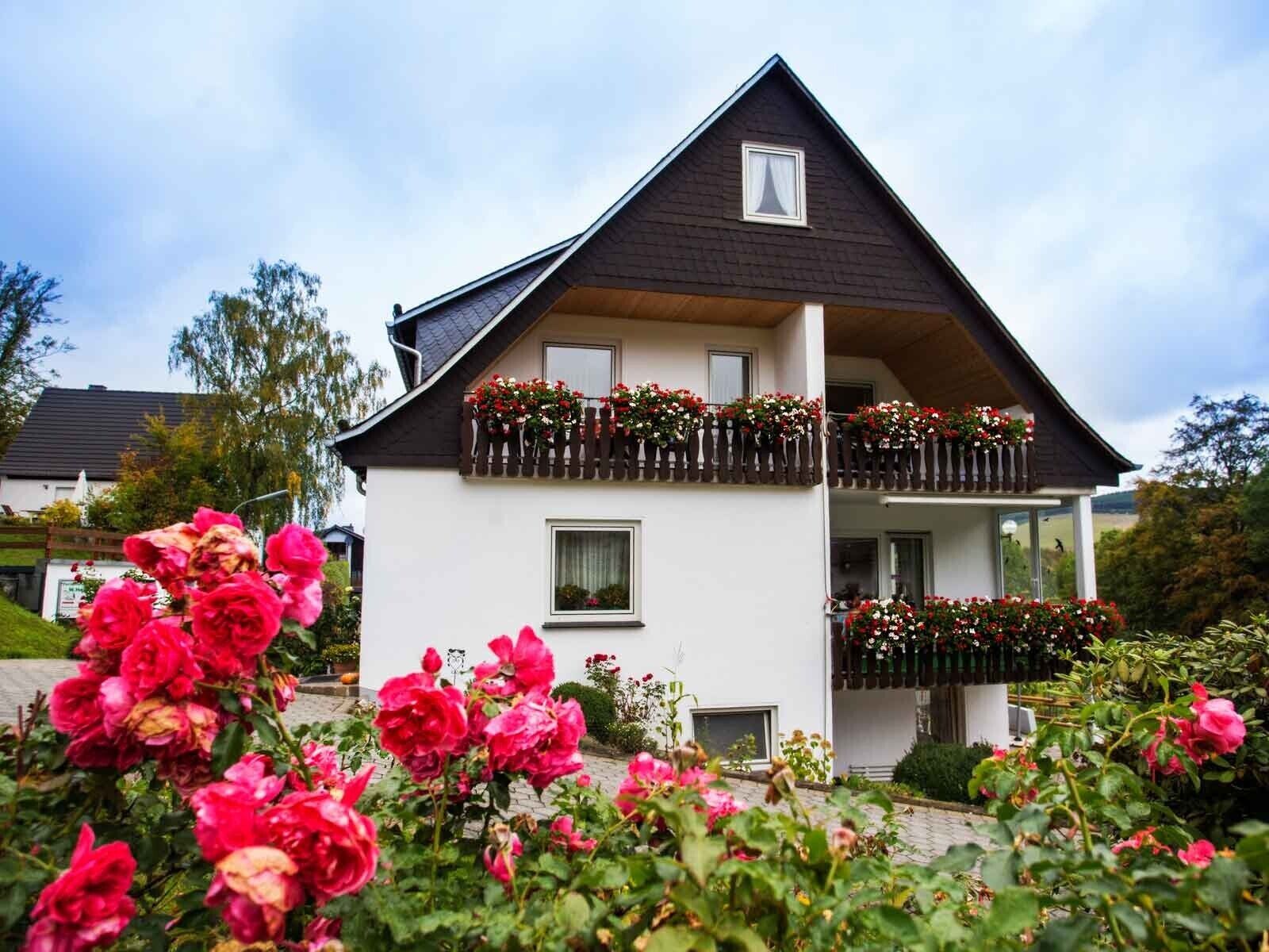 Ein zweigeschossiges Haus mit dunklem Dach und weißen Wänden, mit einem Balkon mit Blumenkästen und einem kleinen Fenster.