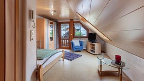 A bedroom with a bed, a glass table, a blue chair, a television, and a window with a view of the outside. - Apartment 'Schweizer' with Mountain View, Balcony and Wi-Fi (Bernau im Schwarzwald)