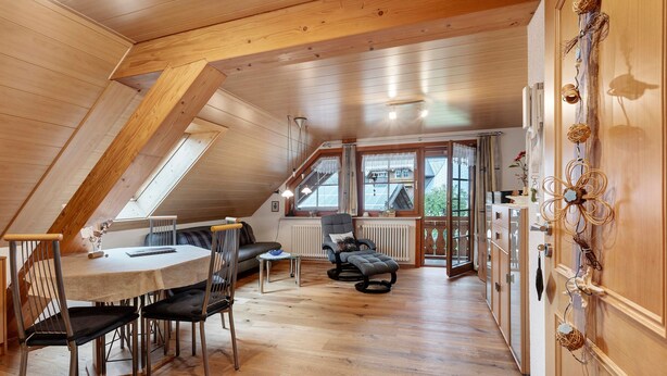A spacious loft with a high ceiling, wooden beams, a dining area with a table and chairs, a sofa, and a view through large windows. - Apartment 'Schweizer' with Mountain View, Balcony and Wi-Fi (Bernau im Schwarzwald)