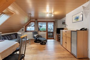 Ein Loft-Zimmer mit Holzbalkendecke, einer Couch, einem Esstisch, einem Fernseher und einem Schrank.