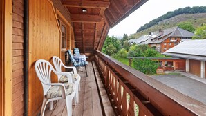 A wooden balcony with white chairs and a table, overlooking a hilly landscape with buildings. - Apartment 'Schweizer' with Mountain View, Balcony and Wi-Fi (Bernau im Schwarzwald)