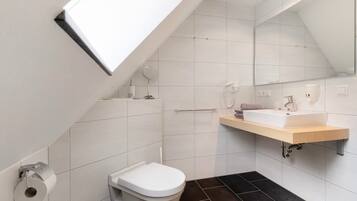 A modern bathroom with a skylight, white tiles, a toilet, a sink, and a mirror.
