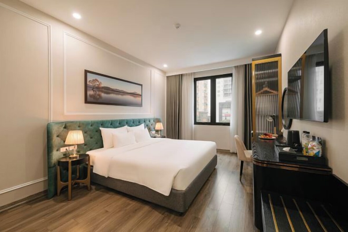A hotel room with a bed, bedside table with lamps, a dresser, a mirror, and a window.