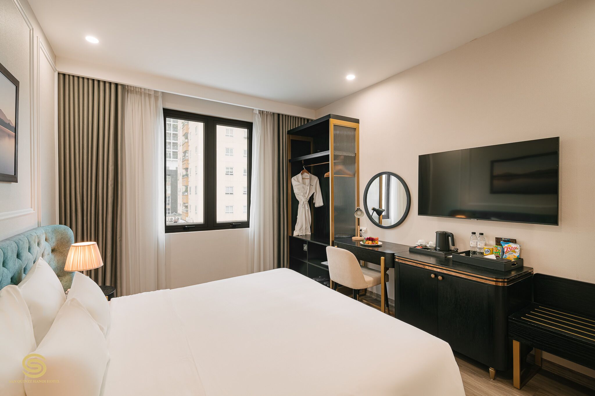 Ein Hotelzimmer mit Bett, Schreibtisch mit Spiegel, Fernseher und Fenster mit Vorhängen.