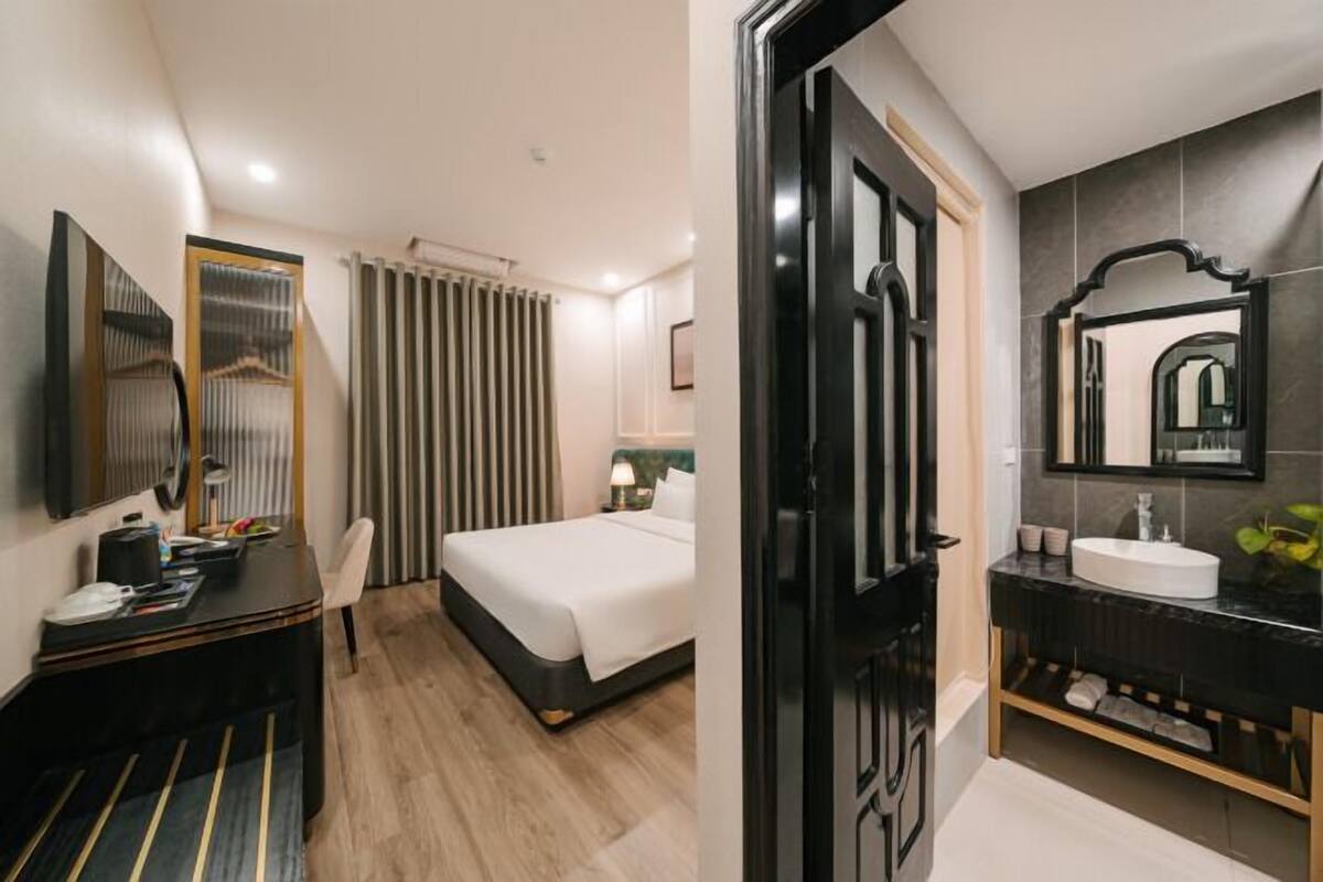 Habitación de hotel con cama, escritorio con silla, espejo y baño con lavabo y espejo.