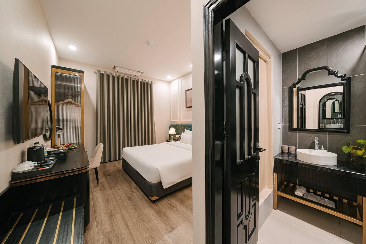 Habitación de hotel con cama, mesita de noche, lámpara y un espejo grande.
